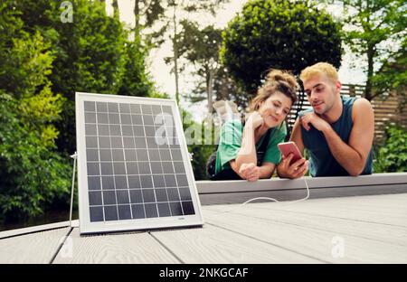 La coppia che condivide lo smartphone è caricata dal pannello solare Foto Stock