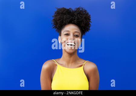 Giovane donna con acconciatura afro ridendo su sfondo blu Foto Stock