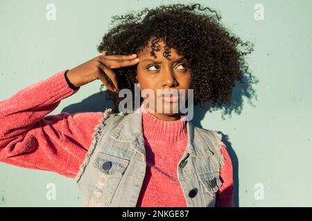 Giovane donna che punta le dita sulla testa di fronte al muro verde Foto Stock