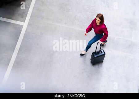 Donna d'affari con bagaglio a rotelle che cammina nel parcheggio Foto Stock