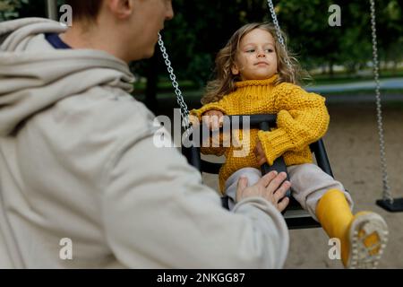 Uomo che spinge la ragazza sull'oscillazione nel parco Foto Stock