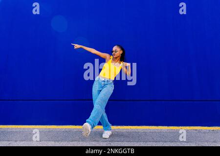 Giovane donna che balla di fronte al muro blu Foto Stock