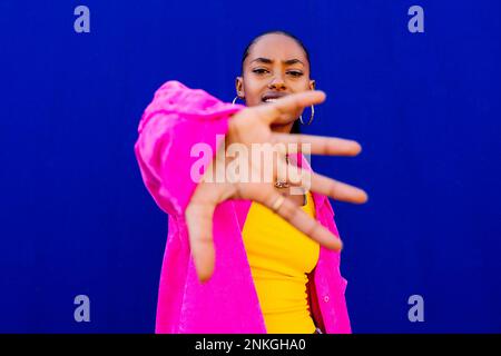 Donna che indossa una giacca rosa gesturante davanti alla parete blu Foto Stock