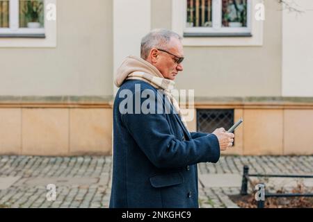 Uomo anziano che usa lo smartphone di fronte all'edificio Foto Stock