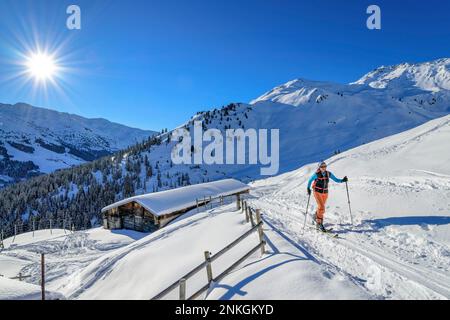 Austria, Tirolo, Sole splendente sulle sciatrici femminili passeggiando davanti a un rifugio appartato nelle Alpi Tux Foto Stock