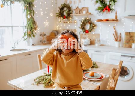 Ragazza che tiene arance sopra gli occhi seduti sul tavolo a casa Foto Stock