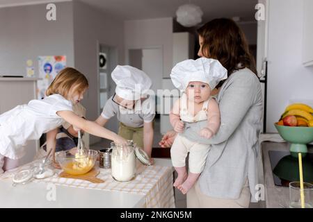 Madre che porta il ragazzo con i bambini che preparano l'impasto in cucina Foto Stock