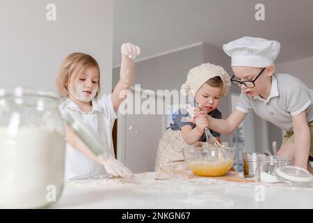 Ragazza che prepara l'impasto con i fratelli mescolando le uova in ciotola a casa Foto Stock