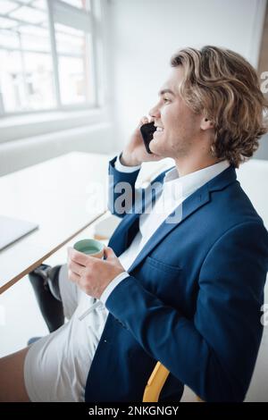 Felice giovane uomo d'affari che parla sullo smartphone in ufficio a casa Foto Stock