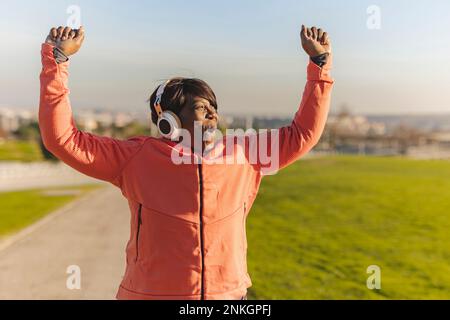 Donna anziana allegra con le braccia sollevate nel parco Foto Stock