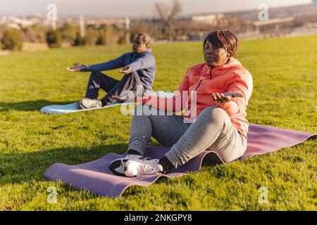 Donna anziana che pratica yoga con l'uomo in background Foto Stock