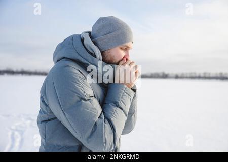 Uomo che indossa un cappello a maglia che scalda le mani in inverno Foto Stock