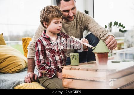Padre aiutare figlio dipingere modello casa a casa Foto Stock