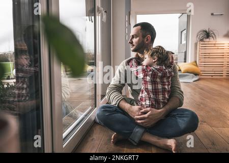 Padre premuroso seduto con figlio sul pavimento a casa Foto Stock