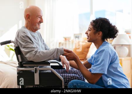 Fisioterapista felice che tiene la mano dell'uomo anziano seduto sulla sedia a rotelle Foto Stock