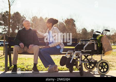 Sorridente custode seduto con un uomo anziano nel parco Foto Stock