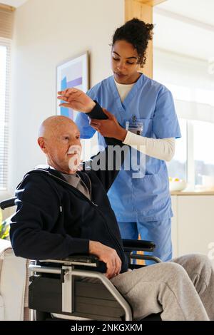 Fisioterapista che aiuta l'uomo anziano su sedia a rotelle con l'esercitazione nel paese Foto Stock