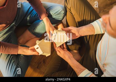 Coppia matura che tiene il modello della casa seduta a gambe incrociate a casa Foto Stock