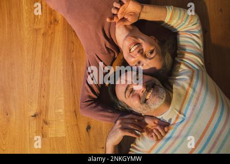 Coppia sposata sorridente sdraiata sul pavimento di legno duro a casa Foto Stock