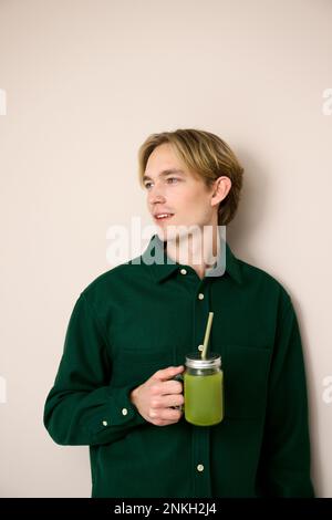 Giovane uomo che tiene frullato verde su sfondo beige Foto Stock