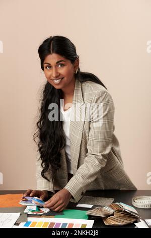 Stilista sorridente in piedi alla scrivania in studio Foto Stock