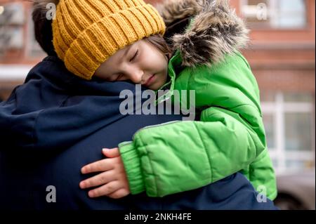 Ragazzo stanco che indossa un cappello a maglia che dorme sulla spalla del padre Foto Stock