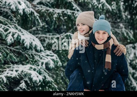 Ragazza sorridente ragazzo piggybacking al parco in inverno Foto Stock