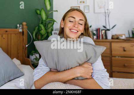 Donna felice con gli occhi chiuso abbracciando cuscino a letto a casa Foto Stock