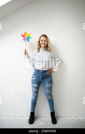 Donna con mano sull'anca che tiene il giocattolo pinwheel in piedi davanti alla parete Foto Stock