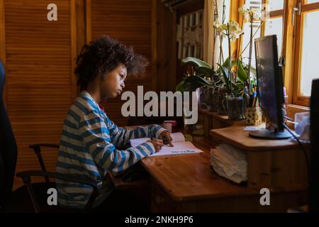 Ragazzo che fa i compiti a casa guardando il computer sul tavolo Foto Stock
