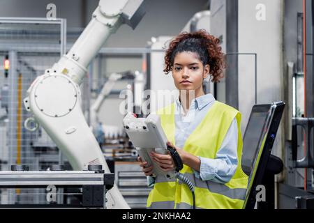 Ingegnere in piedi con l'apparecchiatura davanti al braccio robotico Foto Stock