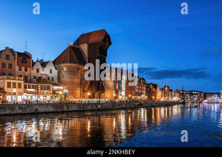 Vecchi edifici e Gdansk Crane Gate di fronte al fiume Motlawa di notte Foto Stock