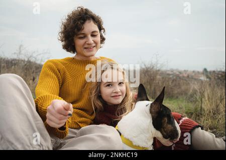 Felice madre e figlia seduta con il cane Bull Terrier Foto Stock