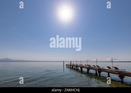 Italia, Veneto, Bardolino, sole splendente su sdraio e ombrelloni su pontile in riva al lago Foto Stock