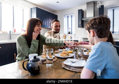 Famiglia felice insieme gustando la prima colazione con le mani impilate al tavolo Foto Stock