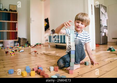 Ragazzo che gioca con i blocchi di giocattoli seduti sul pavimento di legno duro a casa Foto Stock