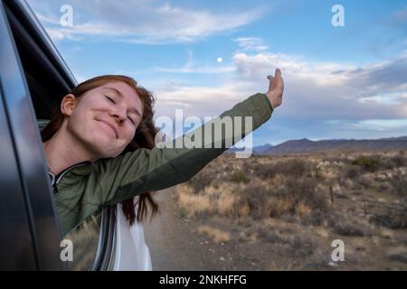 Sud Africa, Provincia del Capo Occidentale, ragazza che si inclina fuori dal finestrino di auto in movimento Foto Stock