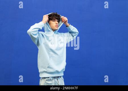 Giovane uomo che indossa una camicia con cappuccio davanti alla parete blu Foto Stock