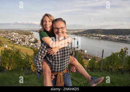 Felice uomo piggybacking donna da fiume sotto il cielo Foto Stock