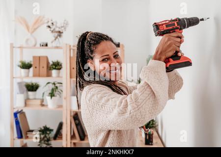Donna sorridente che usa una macchina da trapano a parete a casa Foto Stock