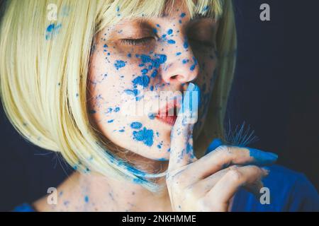 Donna con vernice a polvere blu e dito sulle labbra su sfondo nero Foto Stock
