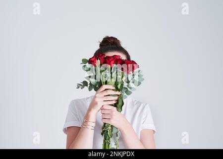 Bello ma pericoloso come la maggior parte delle donne. Studio shot di una donna irriconoscibile che copre il suo volto con fiori su uno sfondo grigio. Foto Stock