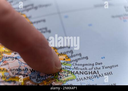 Un dito indica Shanghai, Cina, su una mappa colorata dettagliata con messa a fuoco selettiva, profondità di campo ridotta, sfocatura dello sfondo Foto Stock