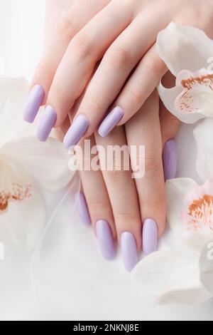 Mani di ragazza con delicata manicure viola e fiori di orchidea. Il concetto di bellezza e cura del corpo. Foto Stock