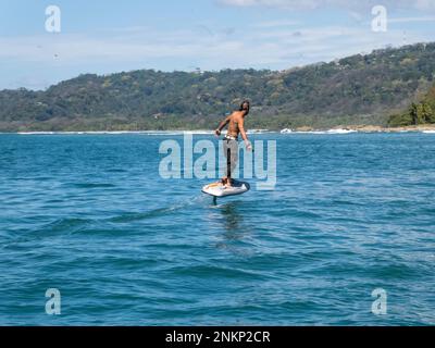 Un uomo guida un e-foil attraverso la superficie dell'acqua vicino alla costa di Malpais Foto Stock