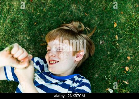 Ragazzo con le lenticelle sdraiate sull'erba, sorridente Foto Stock