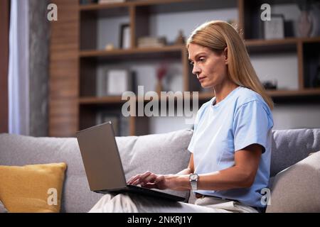 Donna sorridente che usa un notebook, naviga sui siti Web e riposa a casa. Donna freelance fare lavoro online e chattare sul computer mentre si lavora a casa Foto Stock