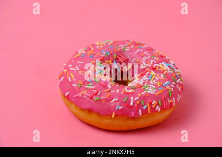 Ciambella con glassa rosa e zucchero multicolore spasles.on sfondo rosa Foto Stock
