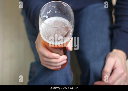 una persona tiene una tazza con birra nella sua mano destra davanti a lui Foto Stock
