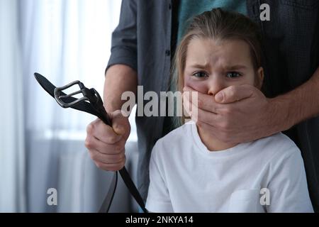 Uomo con la cintura che copre la bocca della bambina spaventato all'interno. Violenza domestica Foto Stock